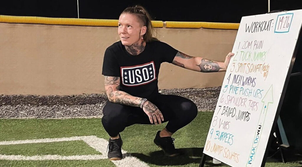 Ali Thompson Explains Why Serving the USO Serves Her as Neatly Ali Thompson Squating Next To A White Board With A USO Workout Plan 1024x567