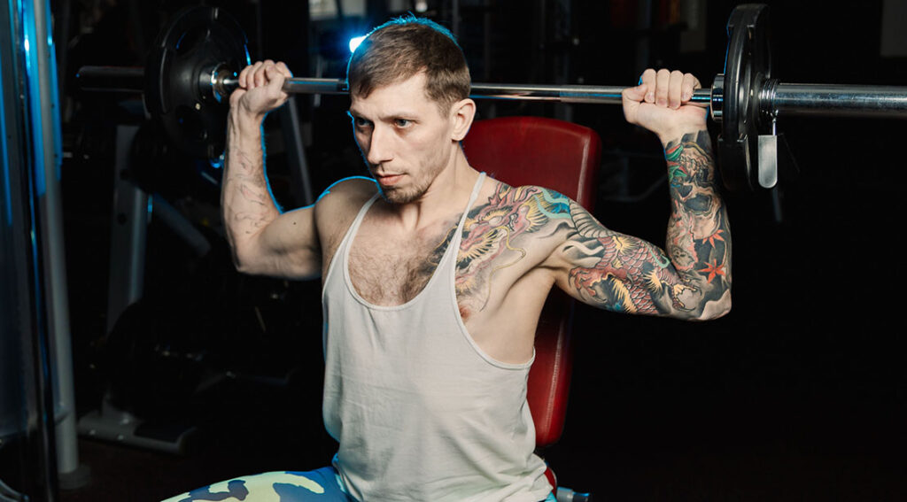 tatooed man and fitness beginner performing the behind the neck barbell press.jpg